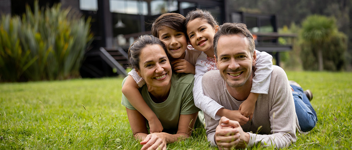 family laying on grass in front of home